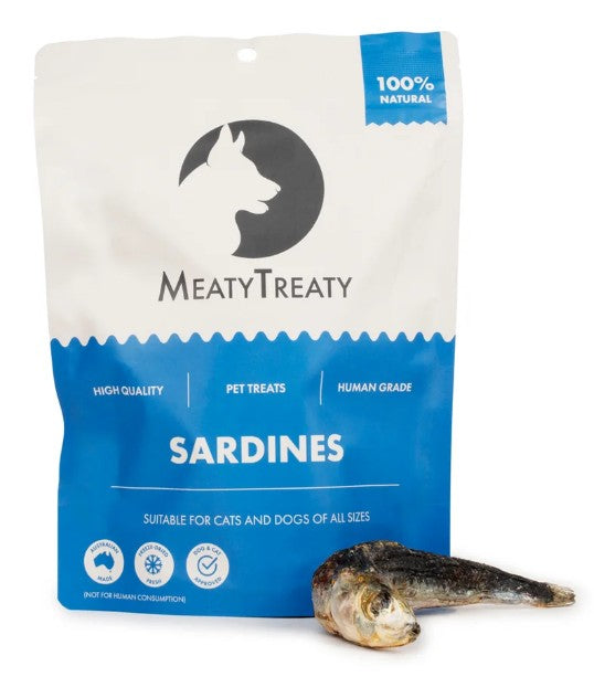 A stand-up pouch of MeatyTreaty Sardines pet treats on a white background, with one whole sardine placed in front of the package.