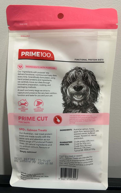 A bag of Prime100 Prime Cut Salmon Treats for dogs, featuring a white and pink design with a black dog illustration, photographed against a neutral gray background.
