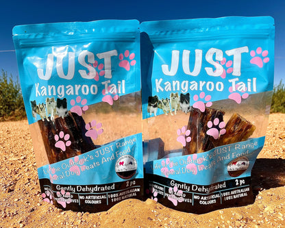 Two packages of 'Just Kangaroo Tail' dog food on a sandy background